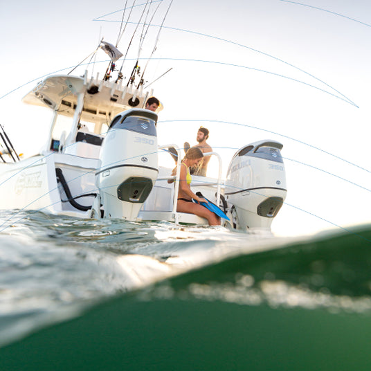 Two Suzuki outboard motors on a boat with three people enjoying a sunny day on the water.